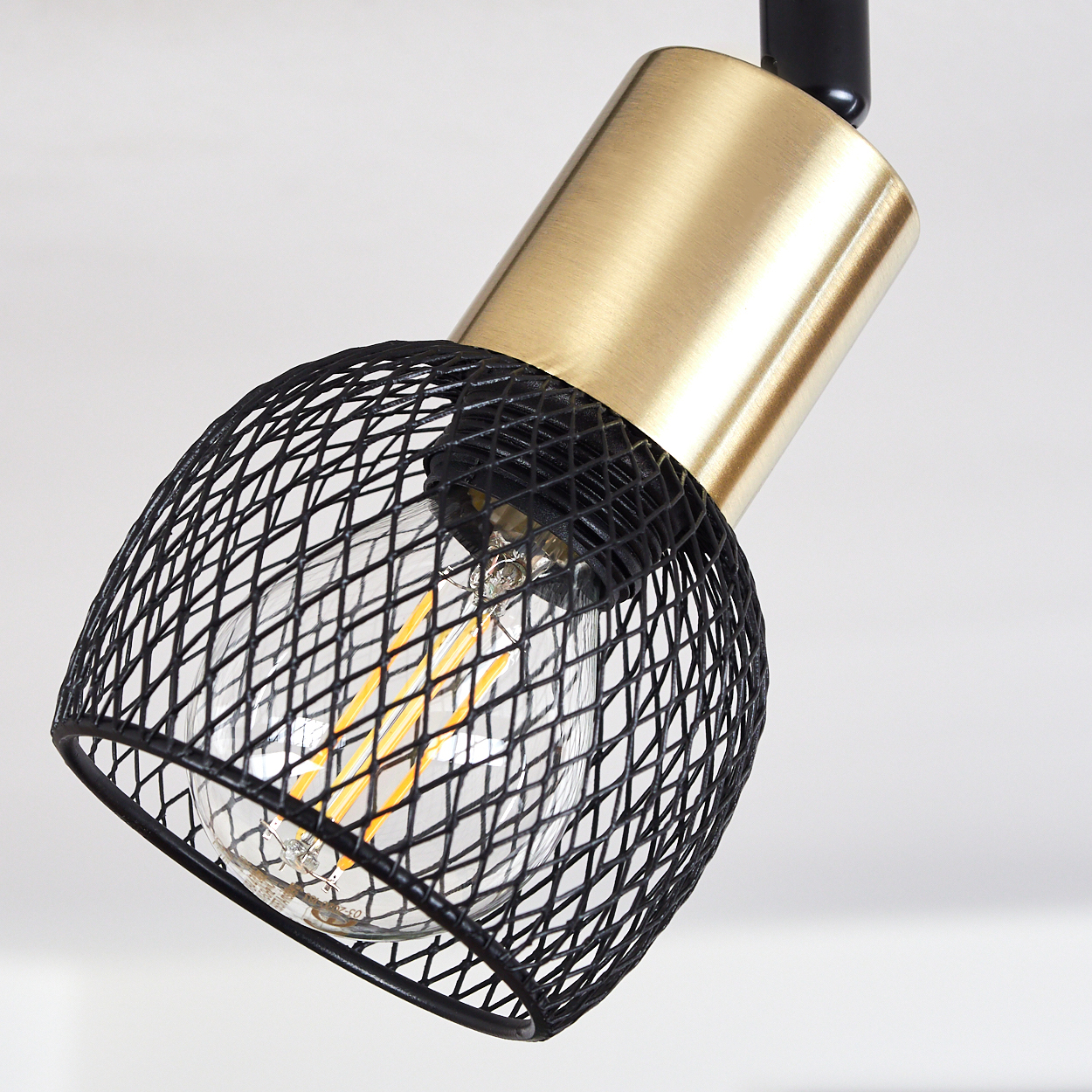 Eine Lampe mit schwarzem Gitter und goldenem Gehäuse vor weißem Hintergrund.