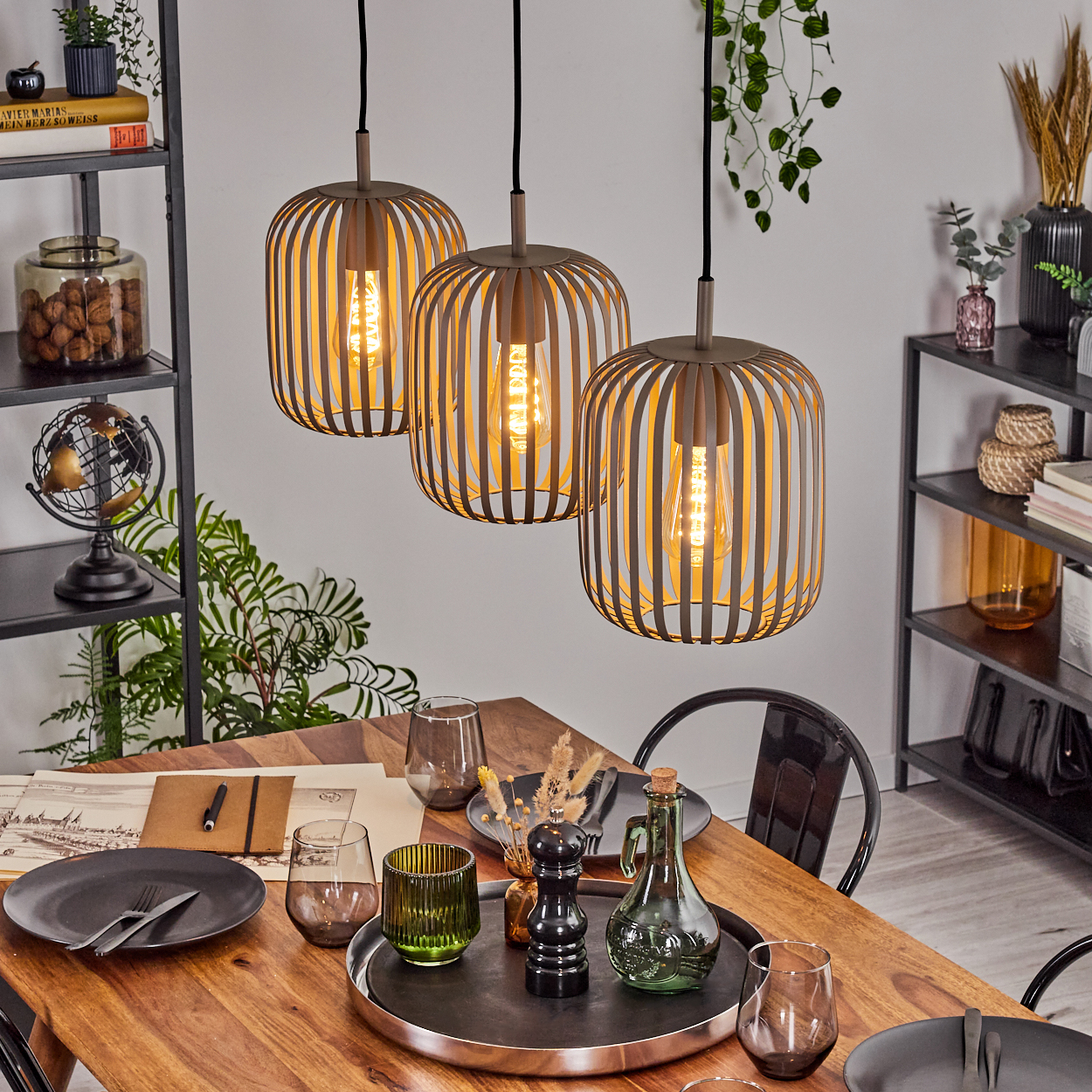 Drei Käfiglampen hängen über einem Holztisch mit Geschirr, Gläsern und Dekoration.