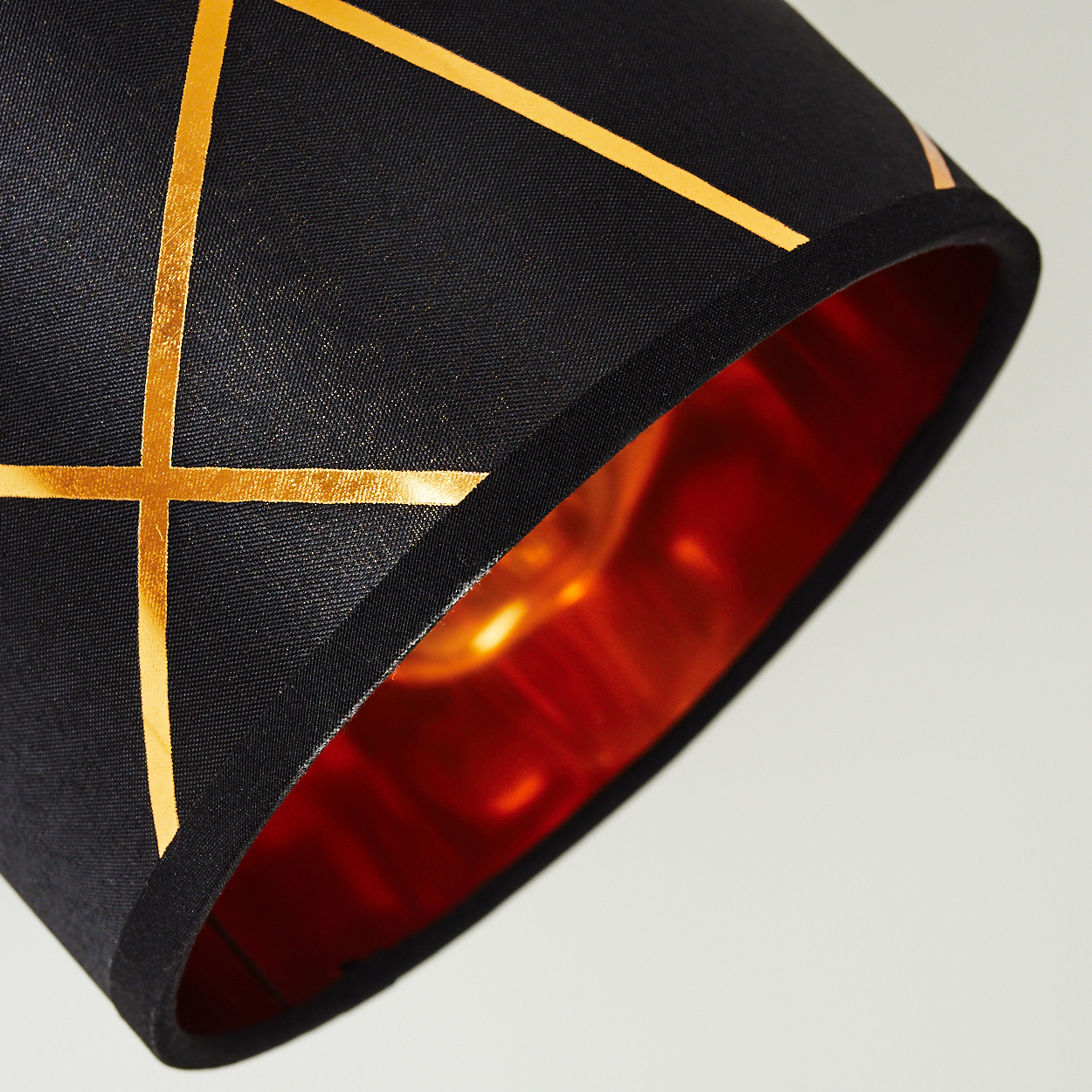 Schwarzer Lampenschirm mit goldenen Linien und kupferfarbenem Innenfutter.