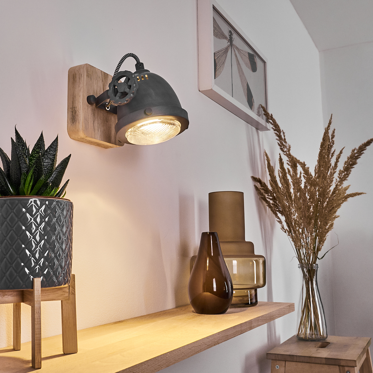 Industrielle Wandlampe über Regal mit Pflanze, Vasen und Trockenblumen.