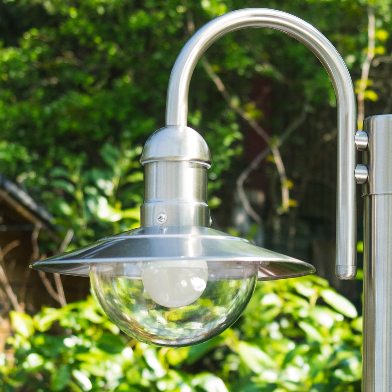 Eine silberne Lampe mit Glaskuppel vor grünen Bäumen.