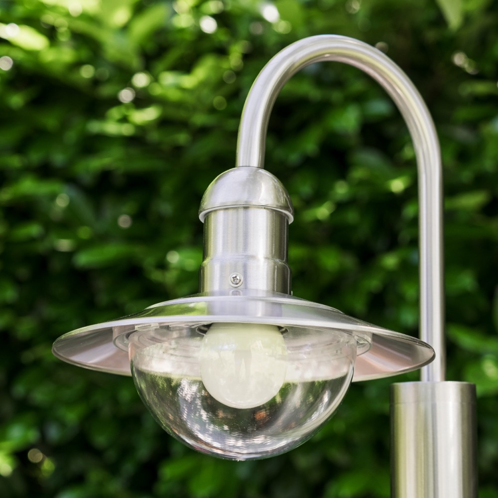 Eine Edelstahl-Gartenlampe mit Glaskuppel vor grünem Laub.