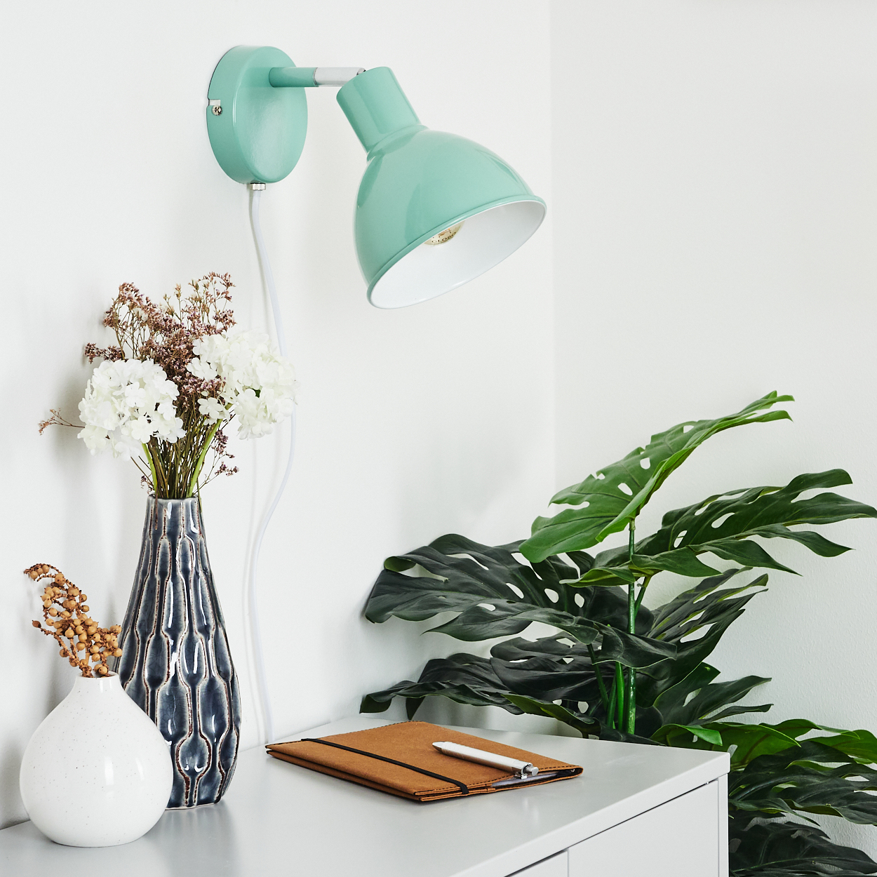 Grüne Lampe an Wand, Vase mit Blumen, Notizbuch auf Tisch.