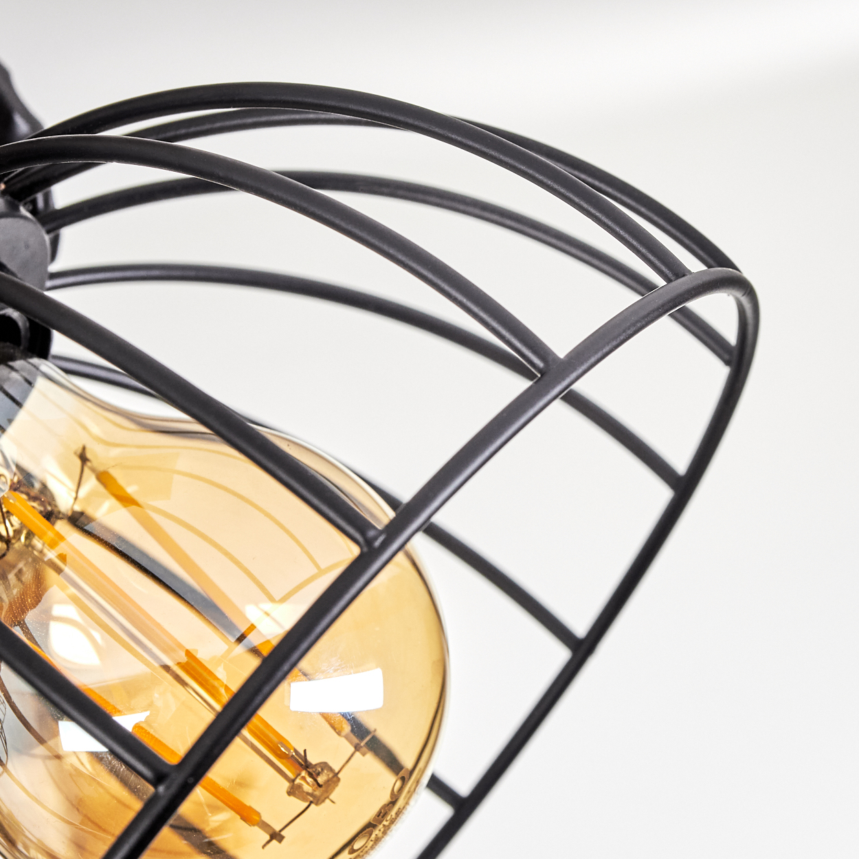 Eine Edison-Glühbirne mit einem schwarzen Drahtkäfig vor weißem Hintergrund.