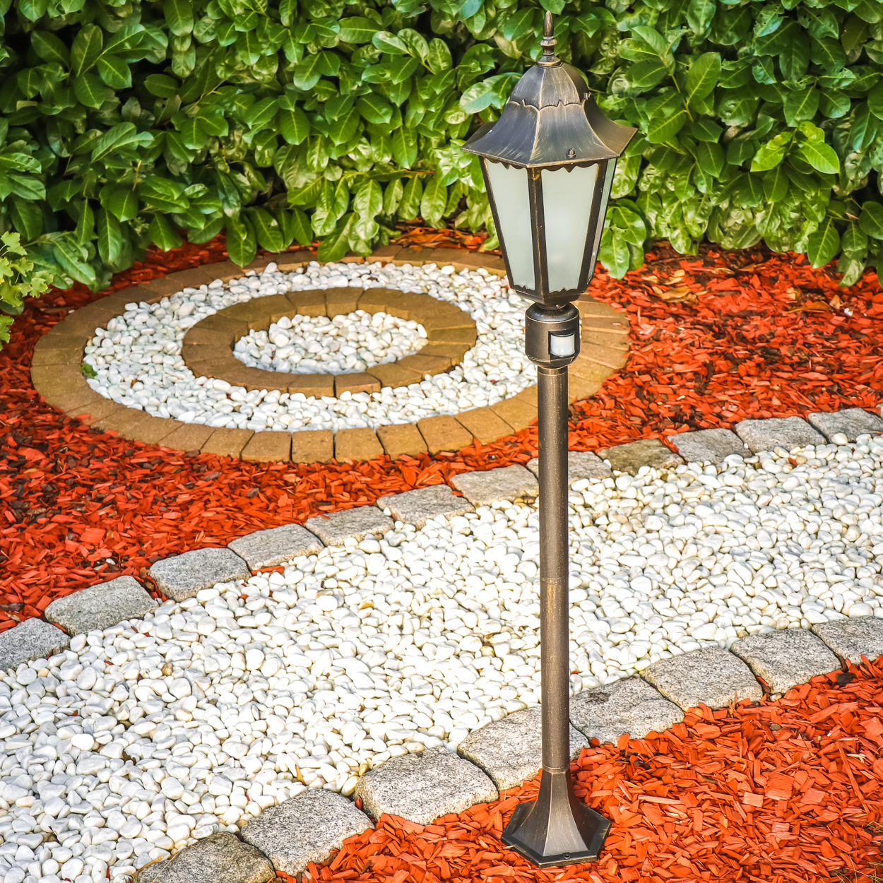 Gartenlampe auf Kiesweg mit rotem Mulch und Steinspiralen.
