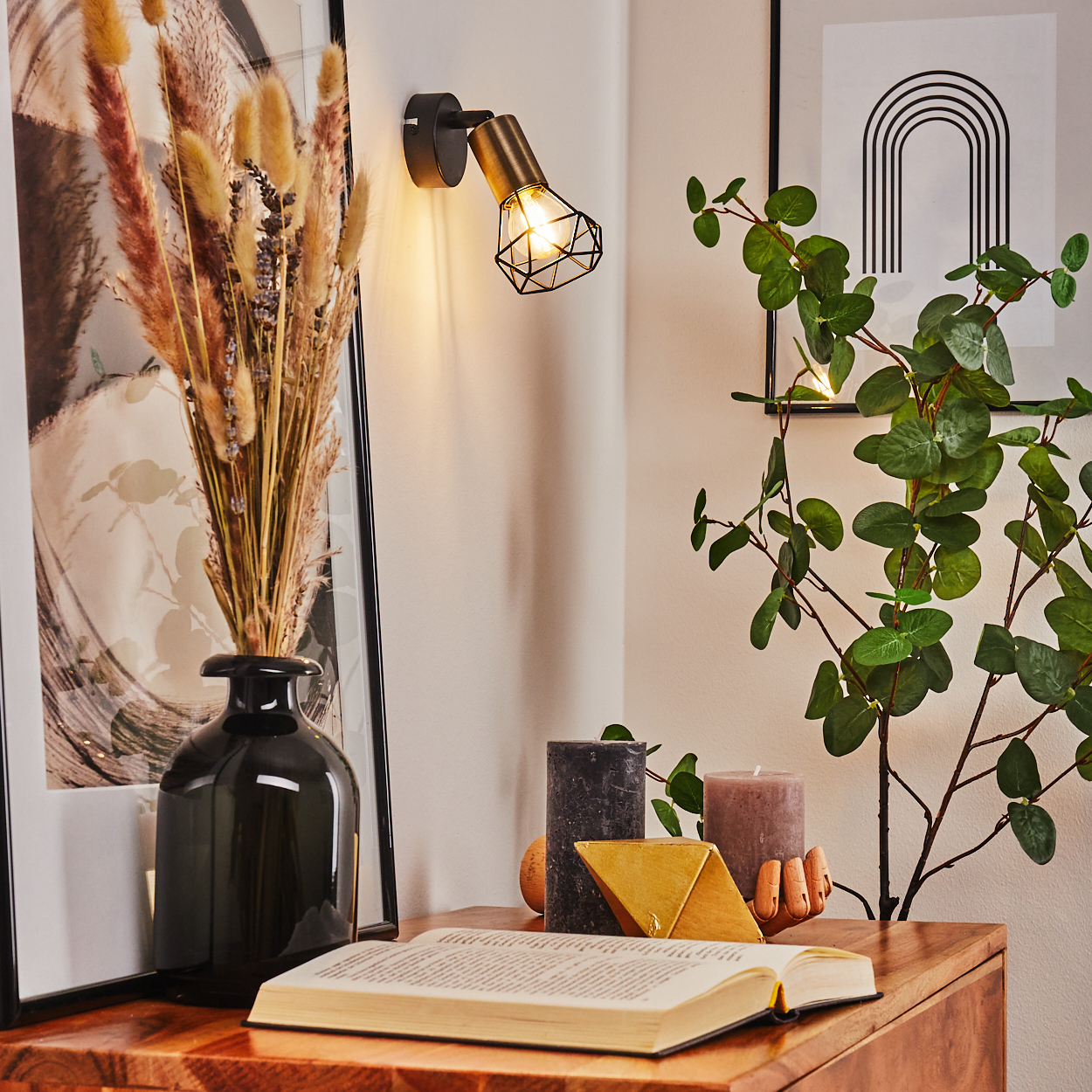 Ein offenes Buch liegt auf einem Holztisch neben einem schwarzen Vase und Trockenblumen.