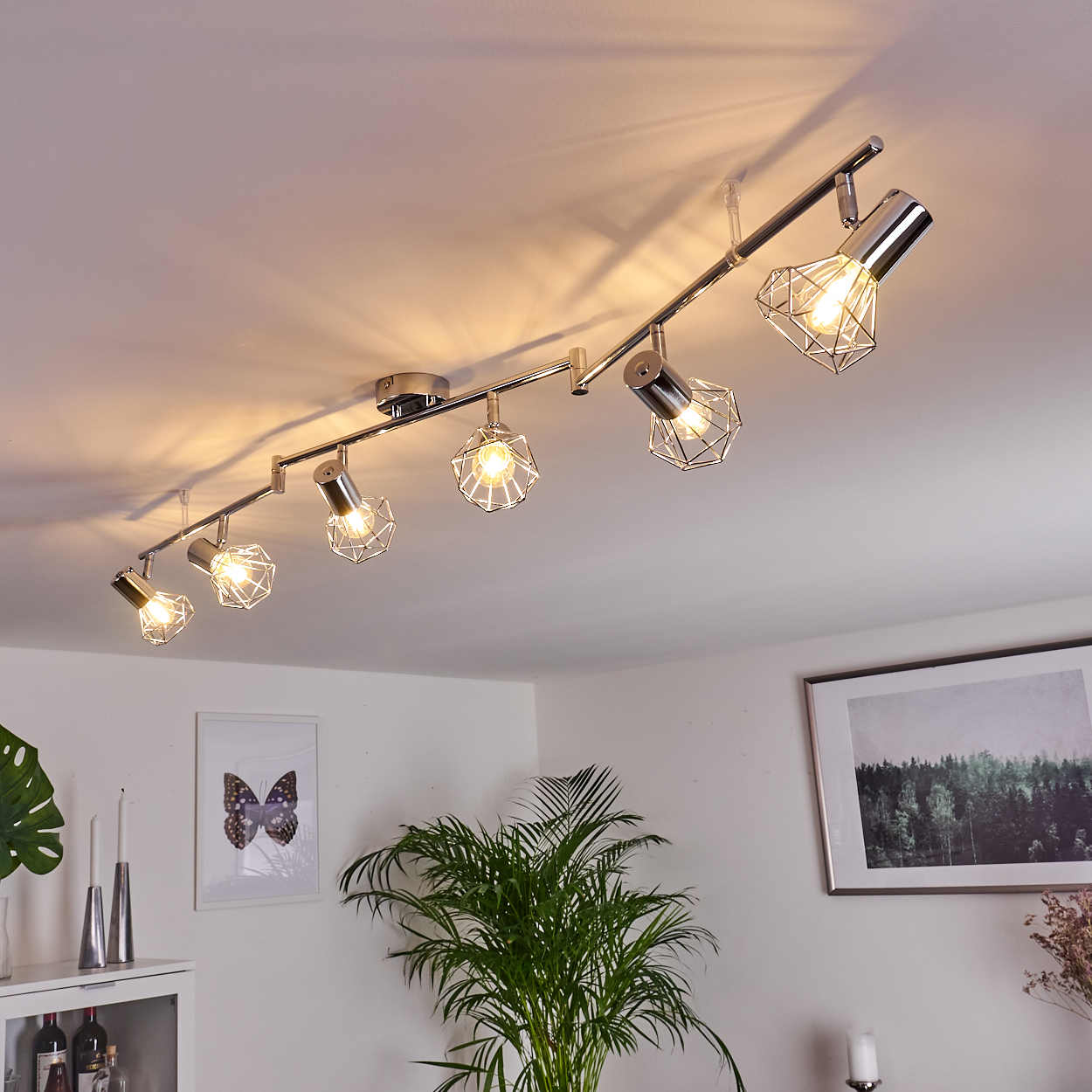 Eine silberne Schienenleuchte mit sechs Lampen, geometrischen Käfigschirmen und Glühbirnen.