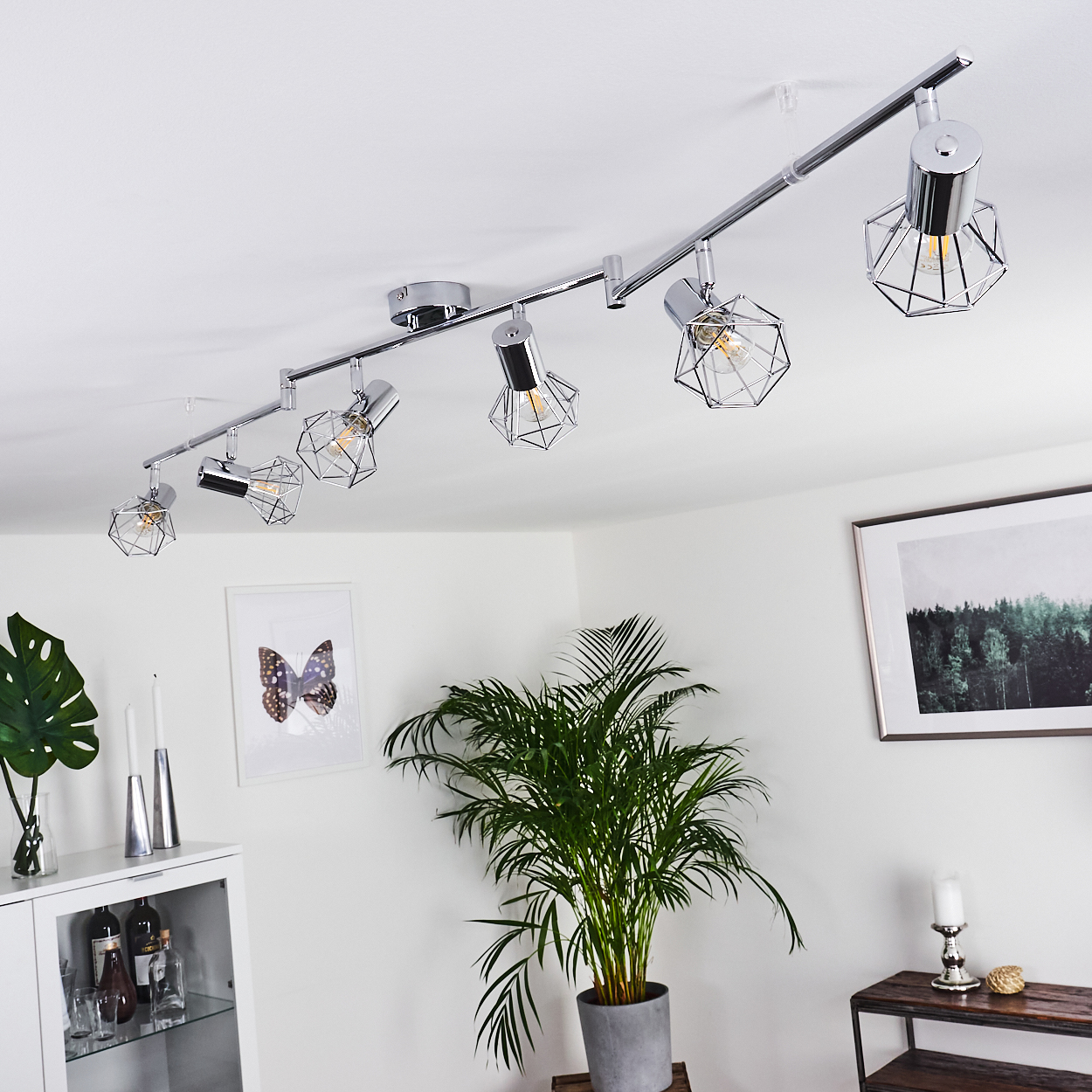 Eine silberne Schienenleuchte mit sechs geometrischen Lampenschirmen an einer weißen Decke.