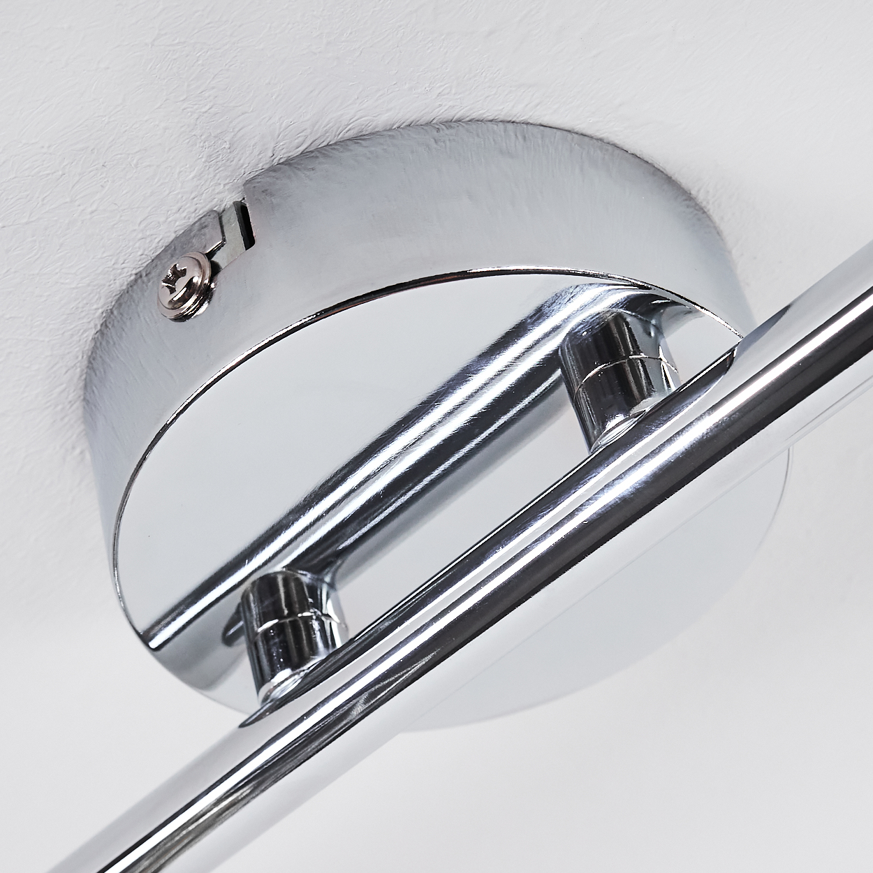 Chromglänzendes Deckenlicht mit silbernem Arm und Schraube an weißer Decke.