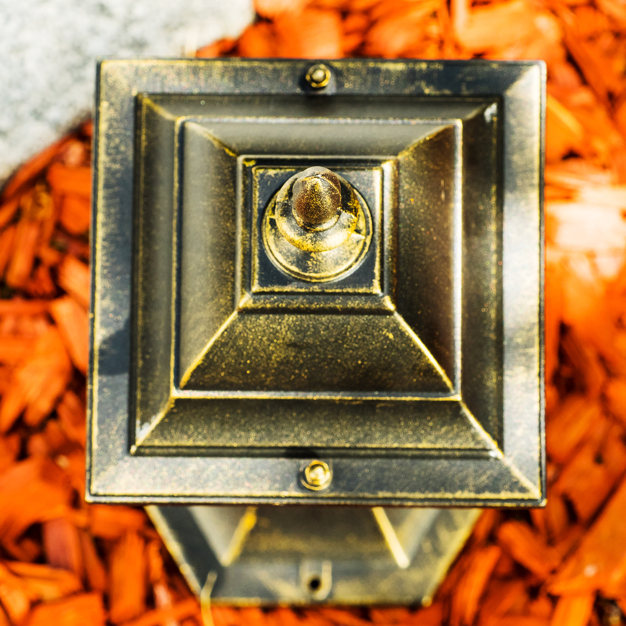 Ein schwarzer und goldener Laternenpfahl-Aufsatz auf orangefarbenem Mulch.