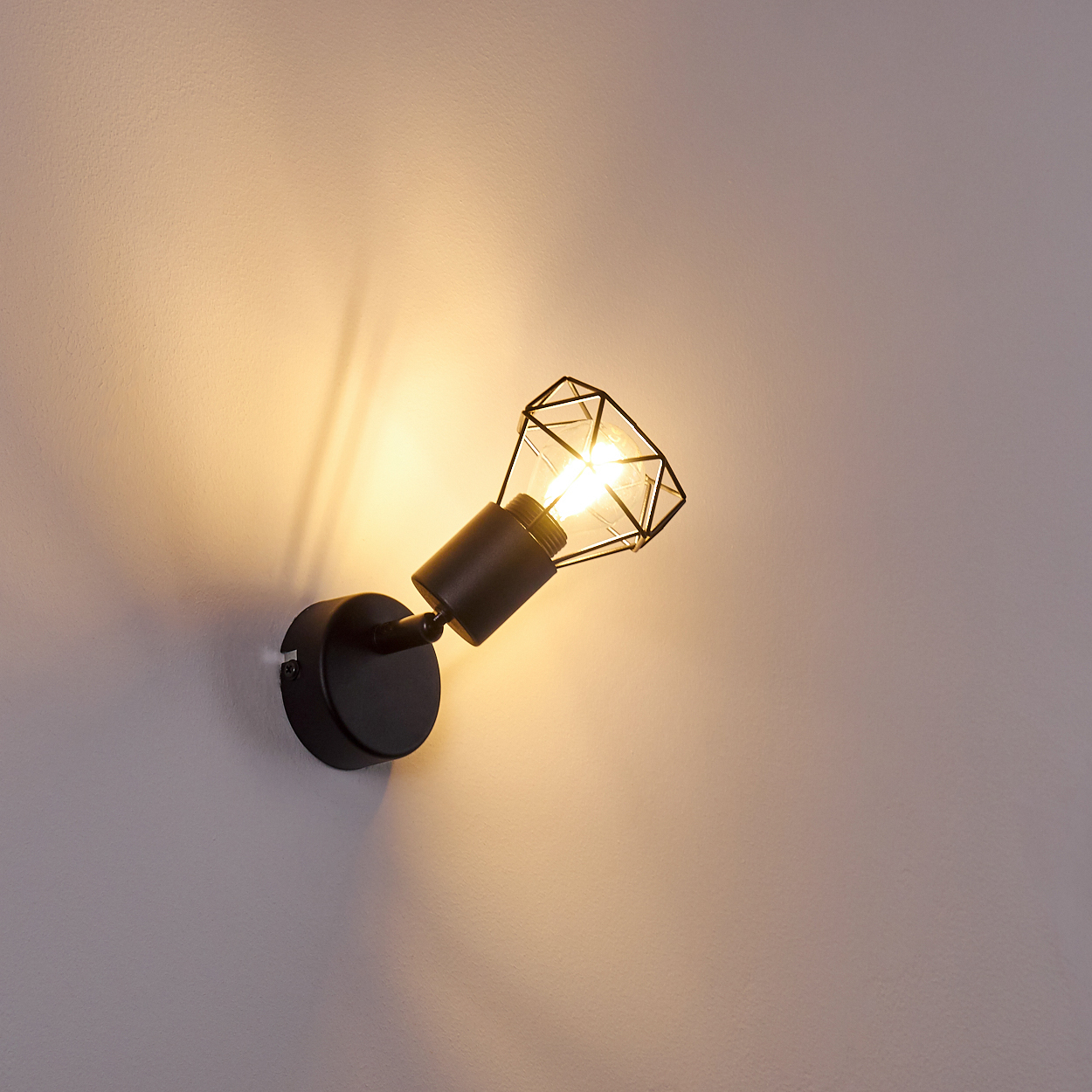 Eine schwarze Wandleuchte mit einem geometrischen Lampenschirm leuchtet gelb.