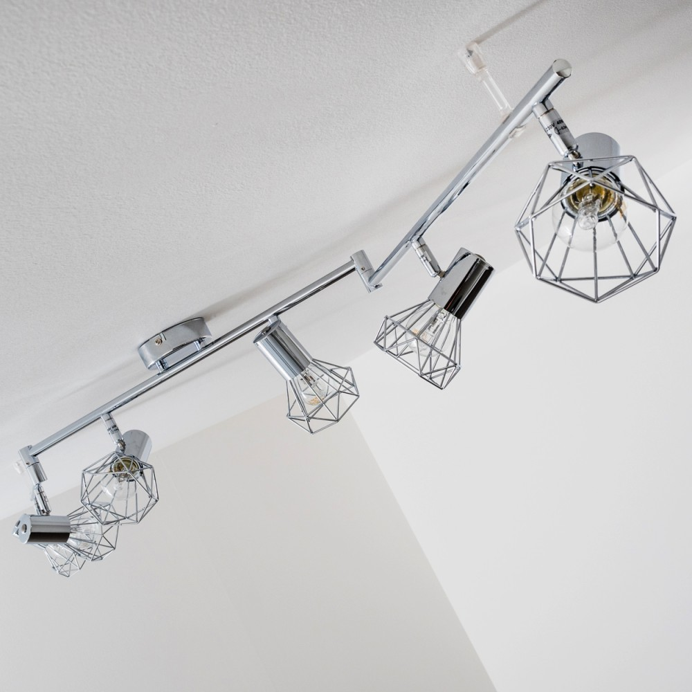 Eine silberne Schienenleuchte mit vier geometrischen Lampenschirmen an einer weißen Decke.