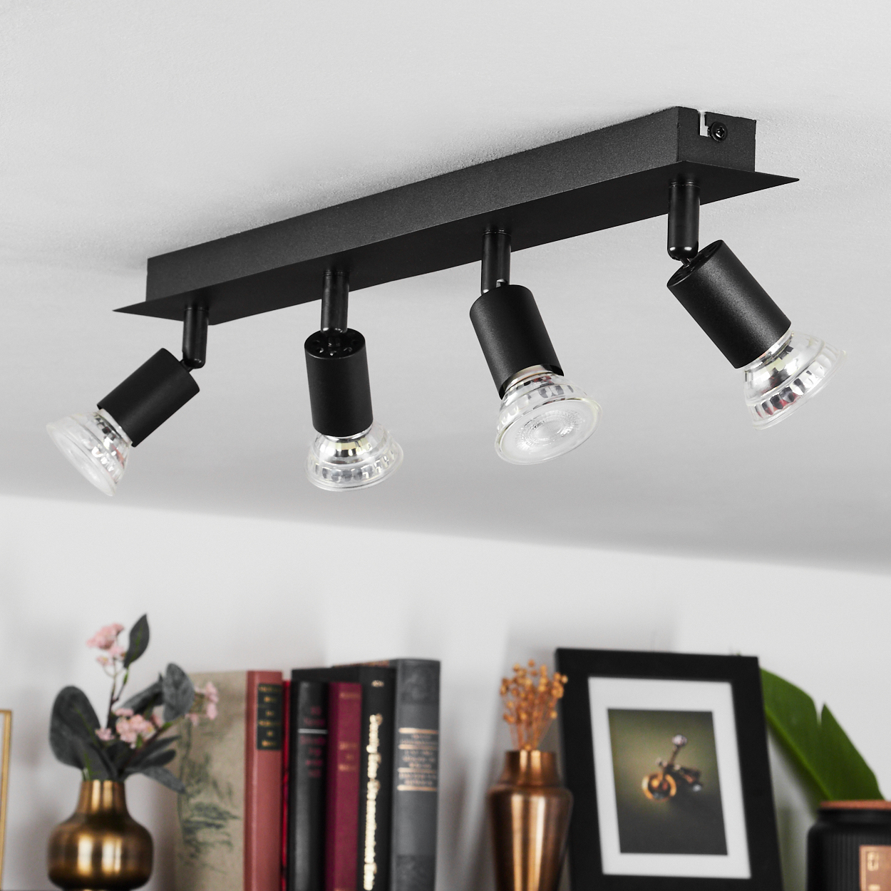 Schwarze Deckenleuchte mit vier verstellbaren Strahlern über einem Regal mit Büchern.
