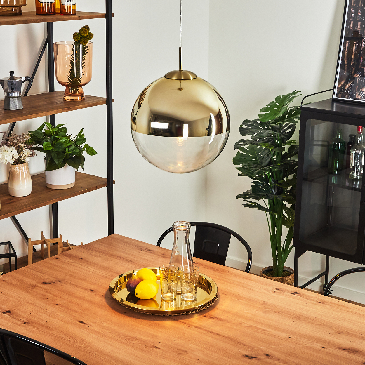 Ein runder goldener Lampenschirm hängt über einem Holztisch mit Obst und Gläsern.