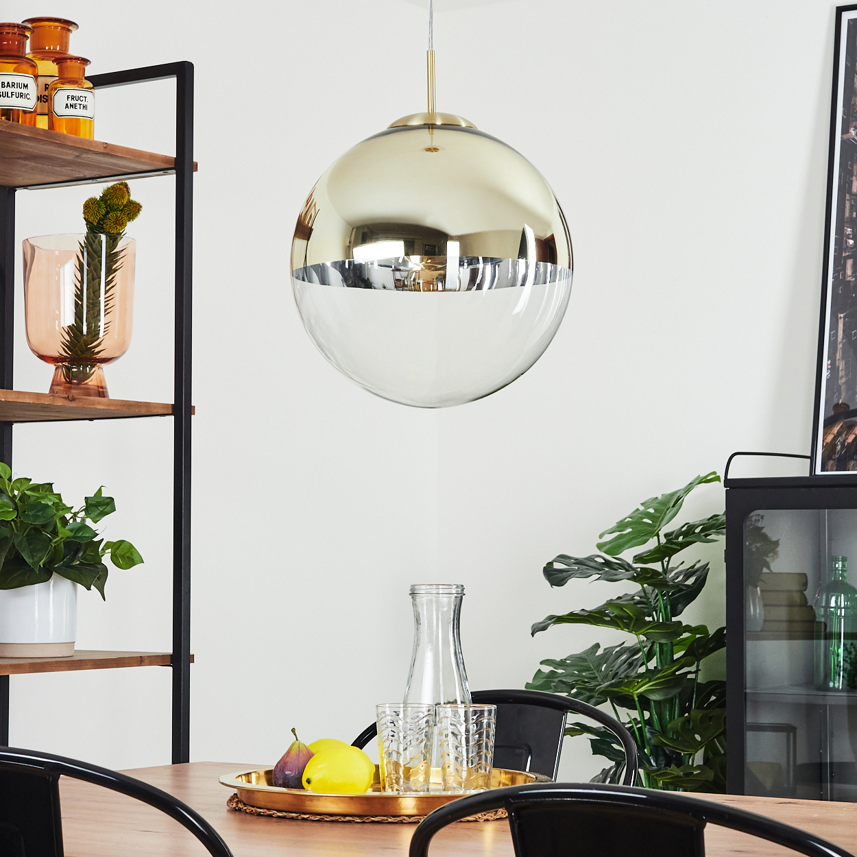 Eine gold-silberne Pendelleuchte hängt über einem Holztisch mit Obst und Gläsern.