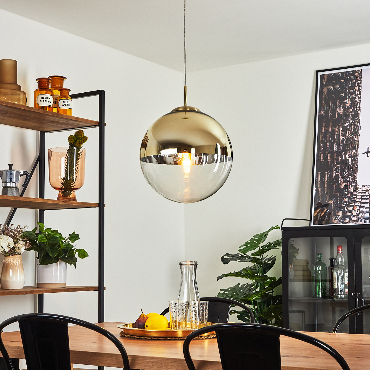 Eine kugelförmige Lampe mit goldenem und klarem Glas hängt über einem Holztisch.