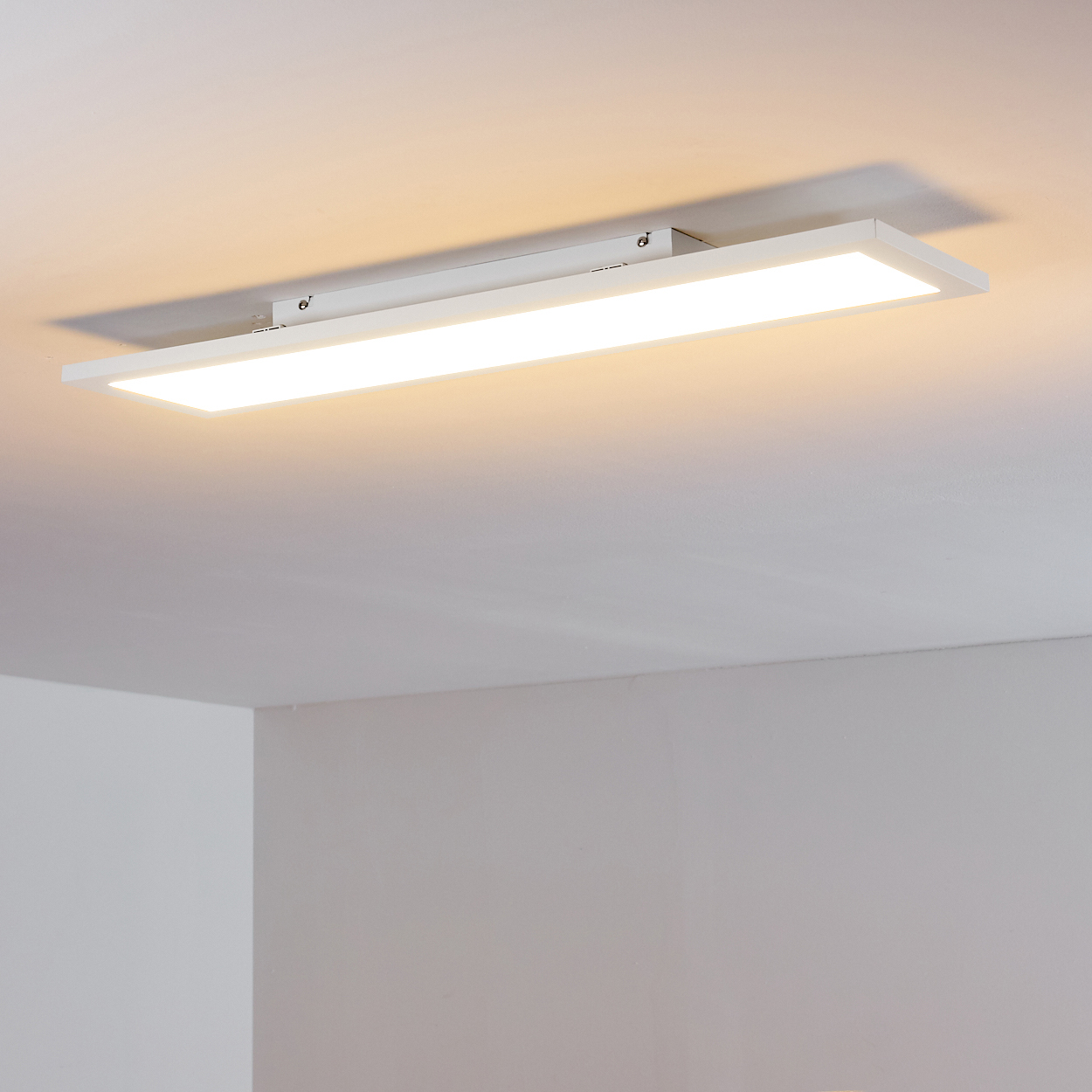Eine weiße rechteckige Deckenleuchte mit hellem Licht wirft einen Schatten an die Decke.