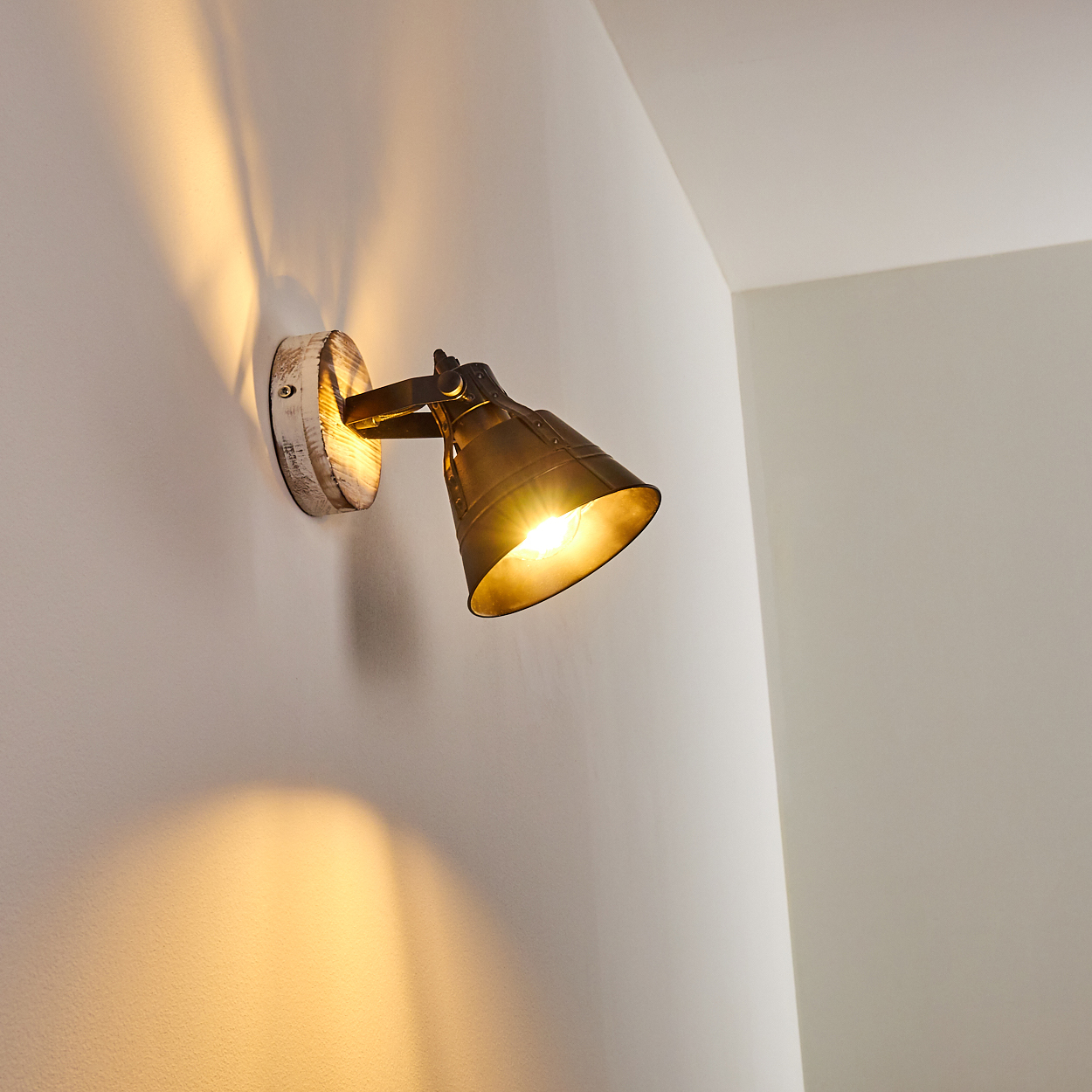 Ein Messing-Wandspot mit Holzsockel beleuchtet eine weiße Wand.