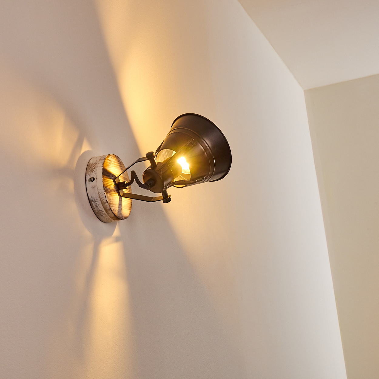 Ein dunkler Wandstrahler mit Holzsockel wirft warmes Licht an die weiße Wand.