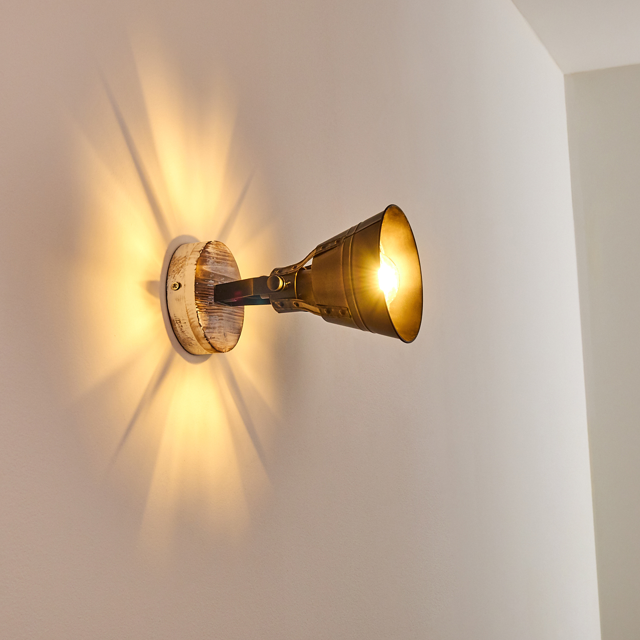 Ein Wandstrahler mit Holzsockel und Metallschirm leuchtet auf einer weißen Wand.
