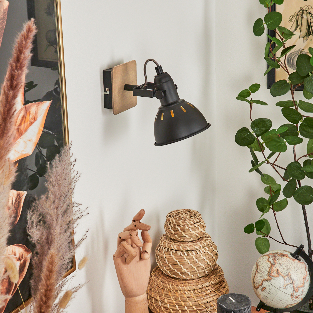 Schwarze Wandlampe mit Holzsockel, daneben ein Holzmodell einer Hand und Körbe.