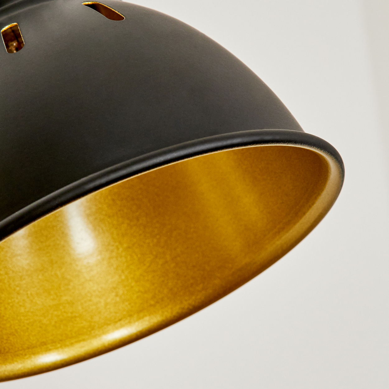 Schwarzer Lampenschirm mit goldener Innenseite und Schlitzen oben.