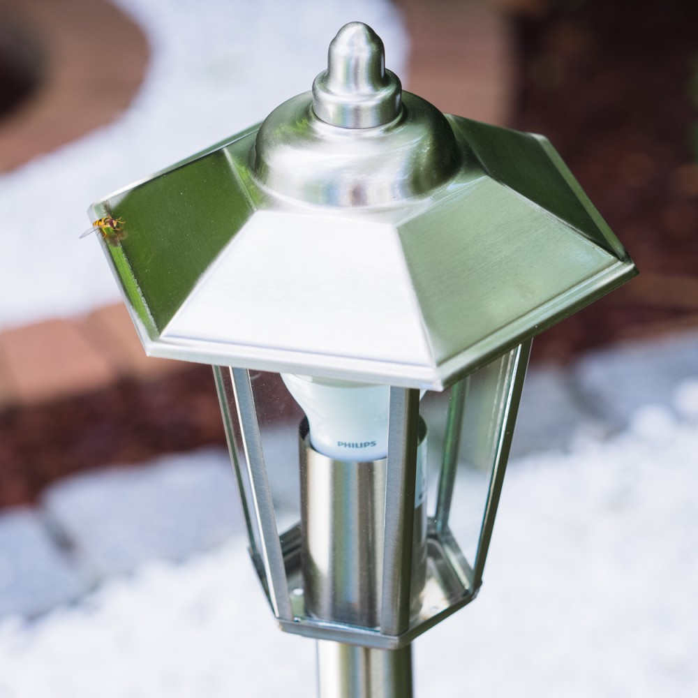 Eine Fliege ruht auf einer Gartenlampe aus Metall mit Philips-Birne. Weiße Steine im Vordergrund.