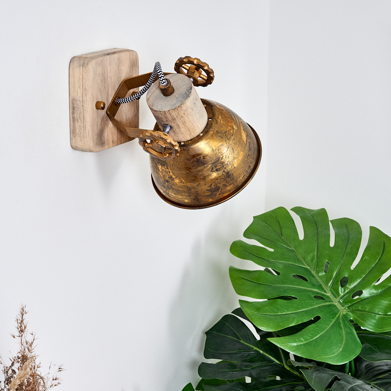 Ein rustikaler Wandstrahler mit Messingglocke und Holzbasis an einer weißen Wand.