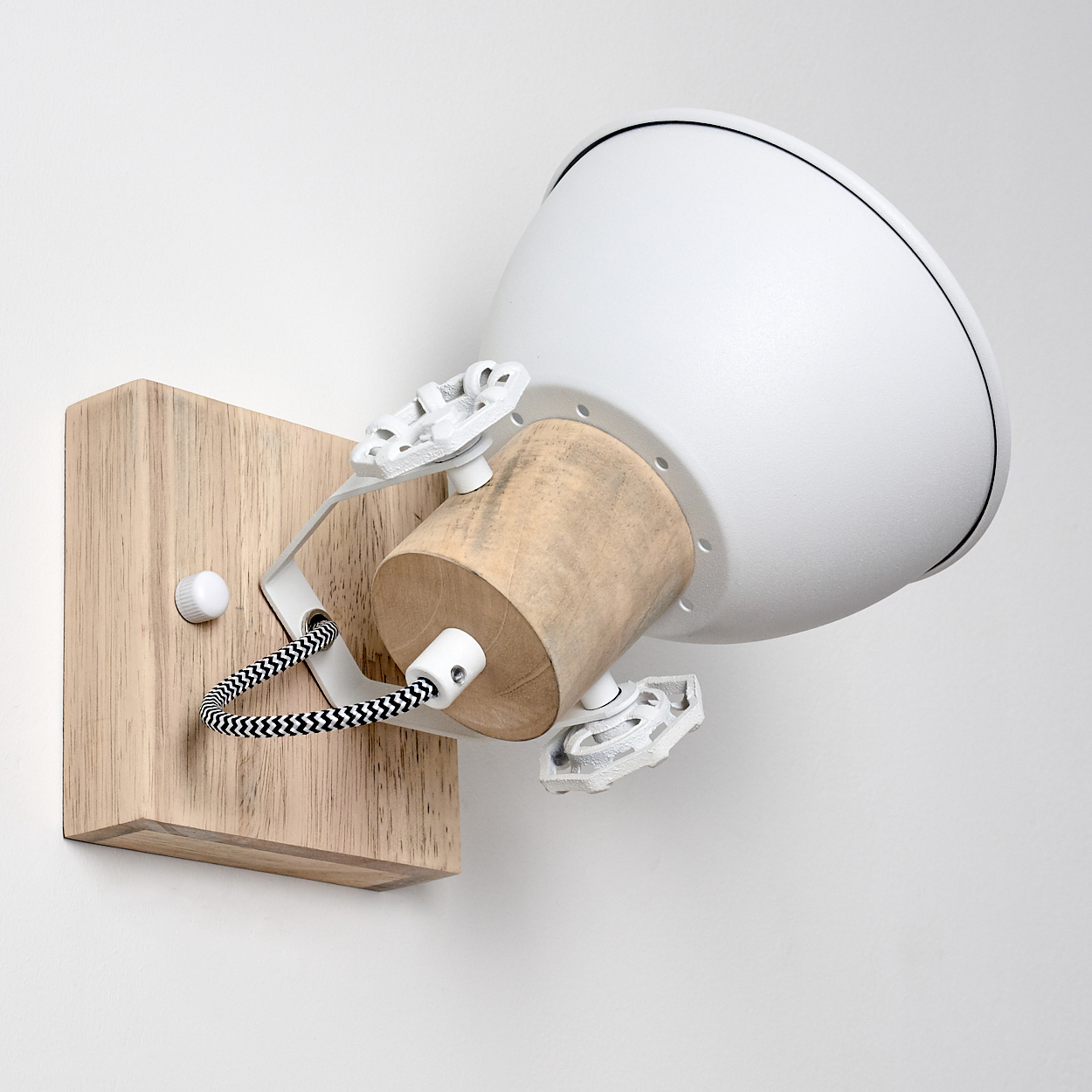 Weiße Lampe mit Holzsockel an der Wand, mit schwarzen und weißen Kabeln.