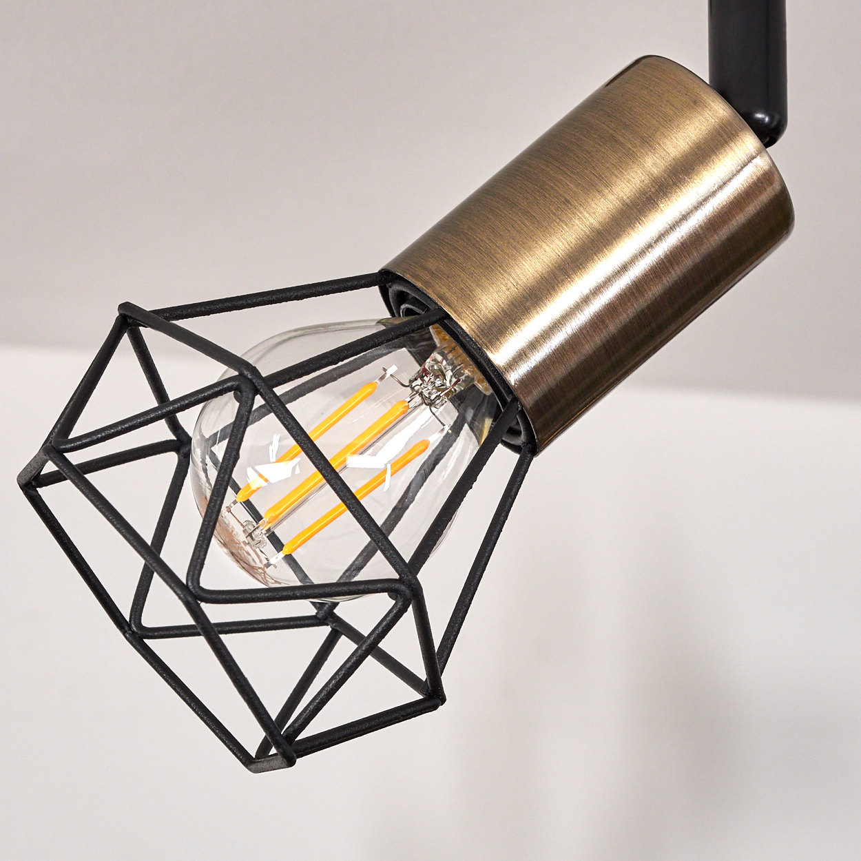 Eine Edison-Lampe mit schwarzem Drahtkäfig und bronzefarbenem Gehäuse.