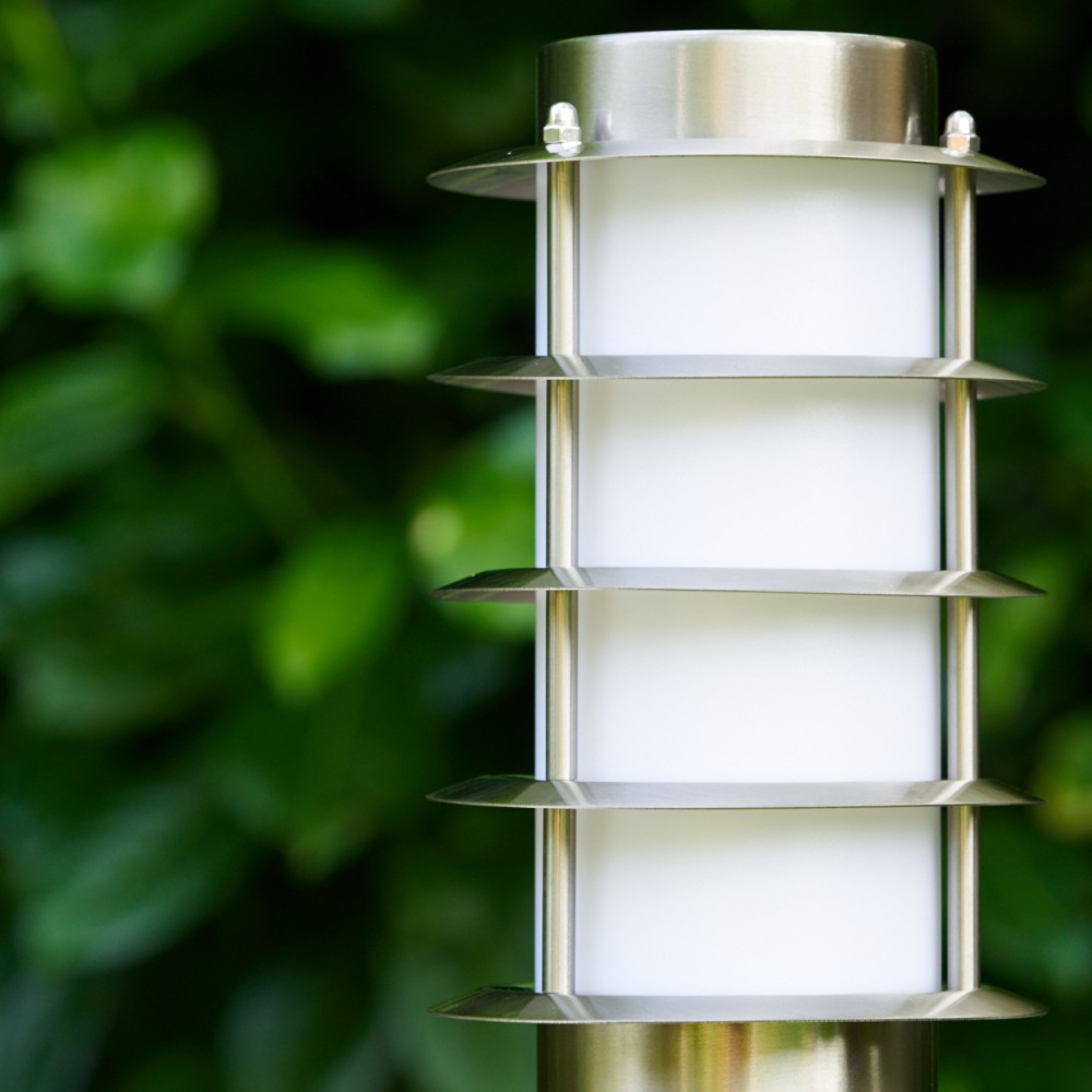 Eine moderne Metalllaterne mit weißen Paneelen steht vor grünen Blättern.