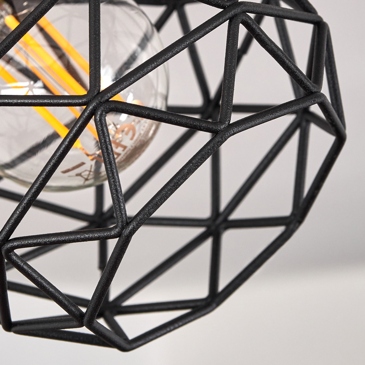 Eine Glühbirne mit orangefarbenen Drähten hinter einem schwarzen geometrischen Drahtkäfig.