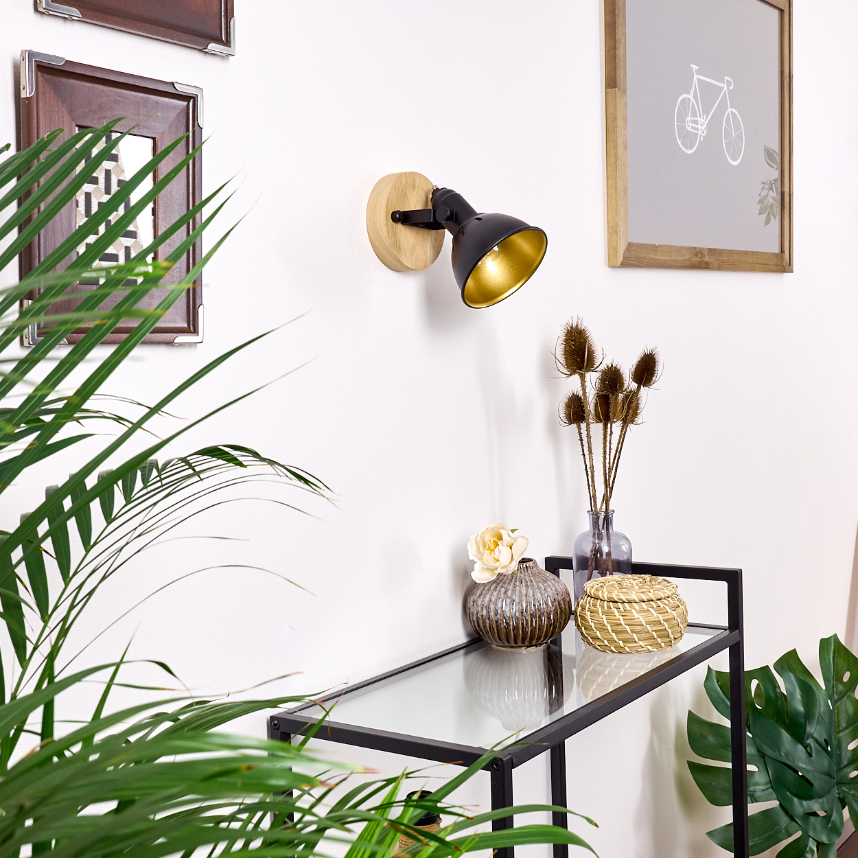 Ein schwarzer Strahler mit goldenem Innerem ist auf einem Holzsockel an einer weißen Wand montiert.