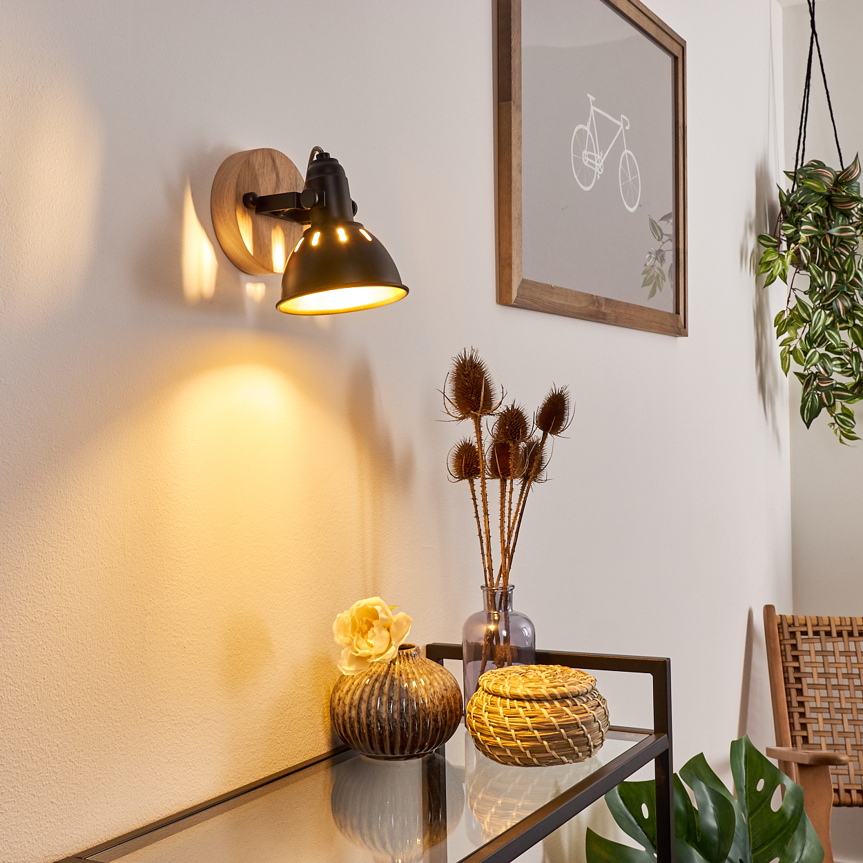 Ein Wandlicht beleuchtet eine Wand über Vasen und Trockenblumen.