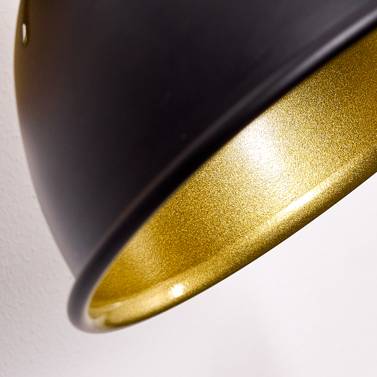 Nahaufnahme einer schwarzen Lampe mit goldenem Rand, die an einer weißen Wand hängt.
