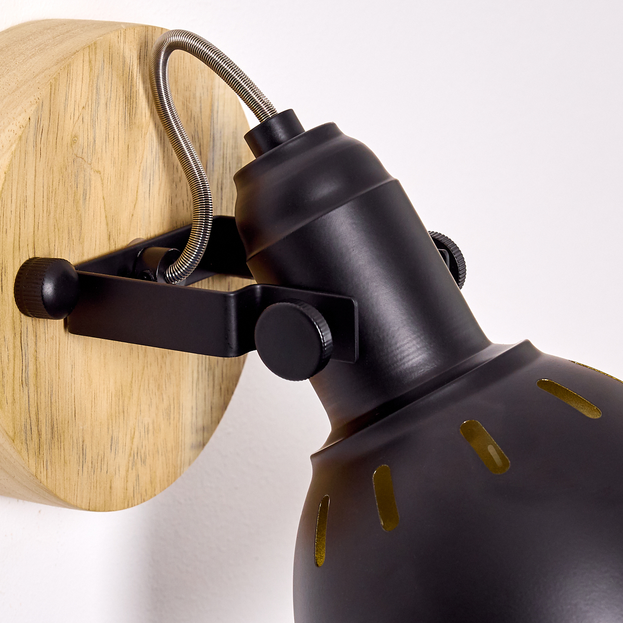 Ein schwarzer Strahler mit flexiblem Arm an einem Holzsockel an der Wand.
