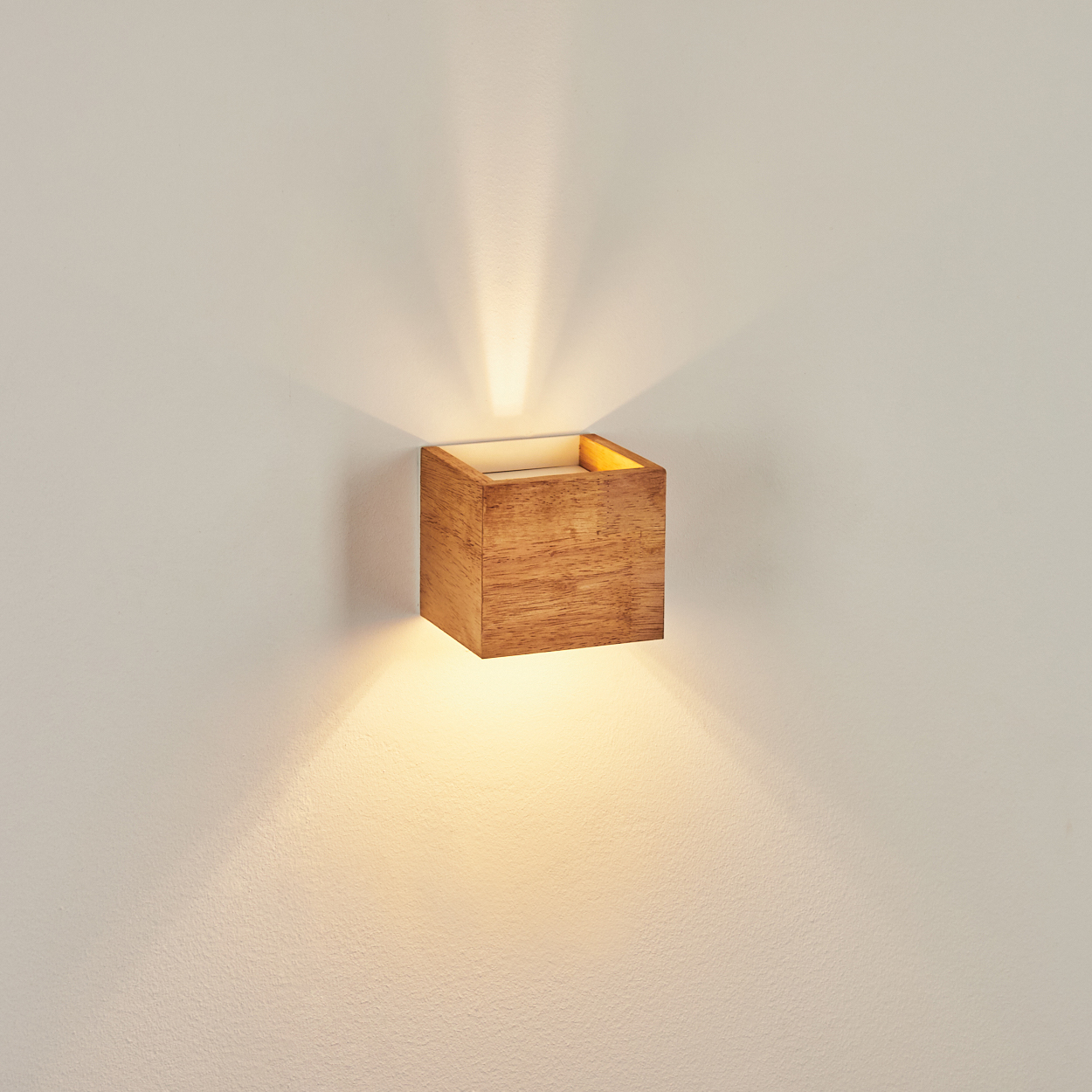 Ein hölzerner Würfel-Wandspot wirft nach oben und unten Licht auf eine weiße Wand.