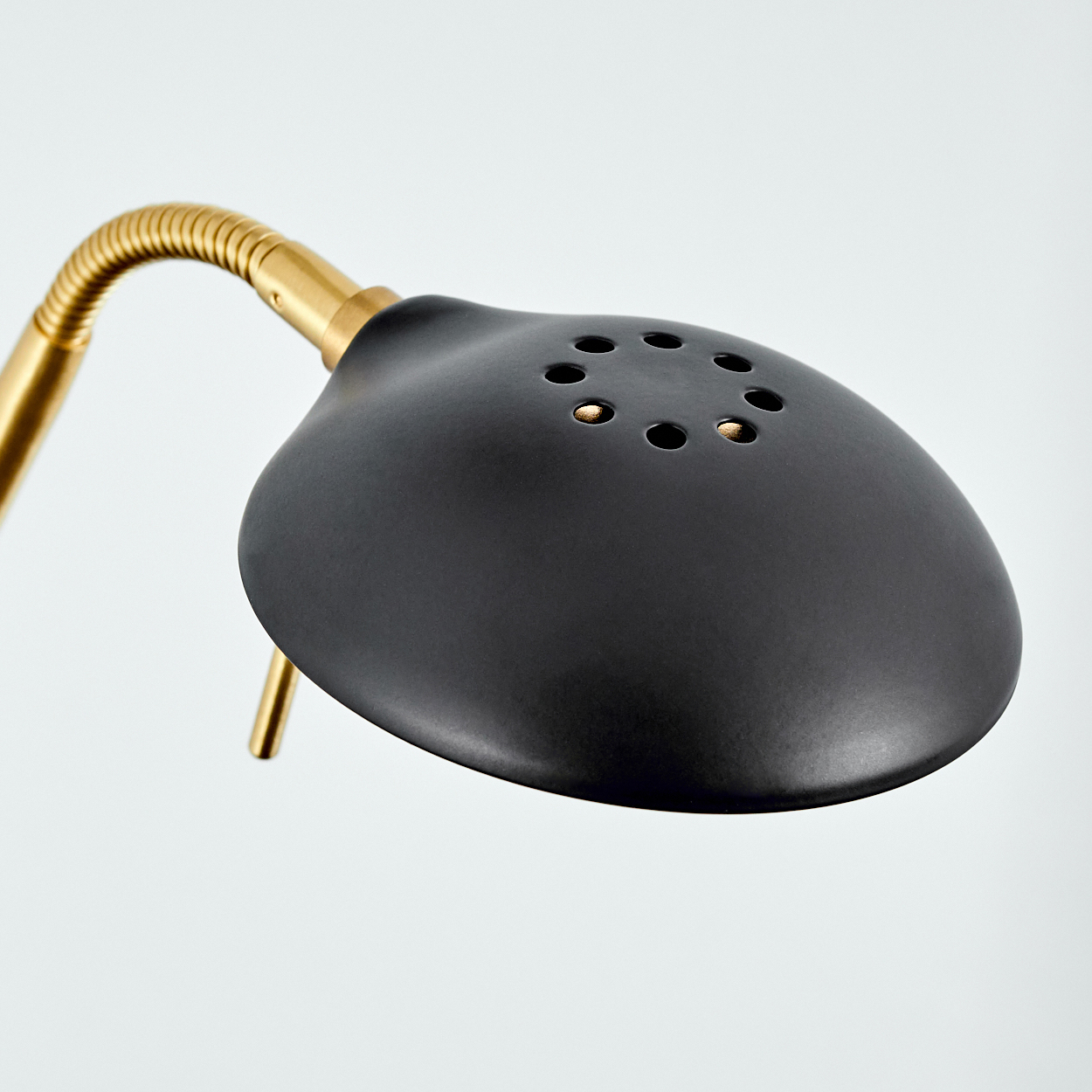 Eine schwarze Lampe mit Messingarm und Belüftungslöchern auf hellem Hintergrund.