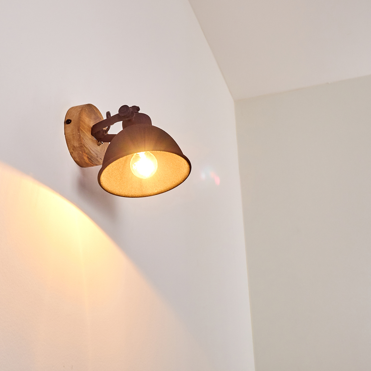 Ein rustikaler Wandspot mit Holzbasis und Metallschirm beleuchtet eine weiße Wand.