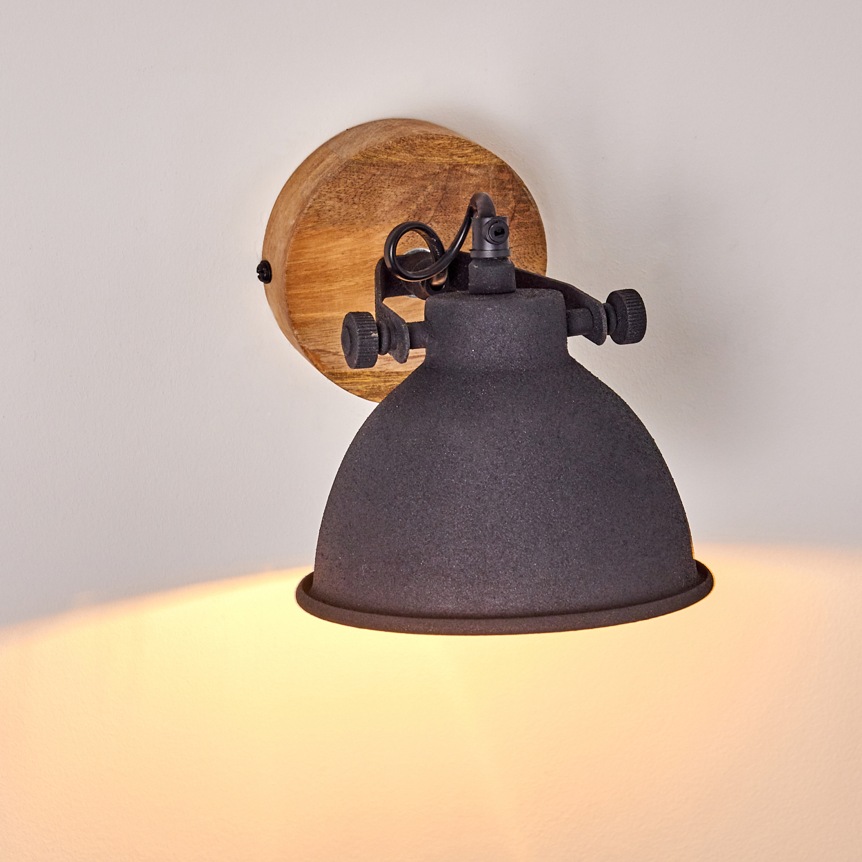 Eine dunkle Wandlampe mit Holzmontage und verstellbarem Arm beleuchtet eine weiße Wand.