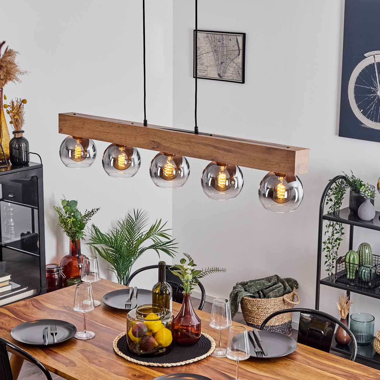 Holz-Hängeleuchte mit fünf Glaskugeln über einem Holztisch mit Geschirr.