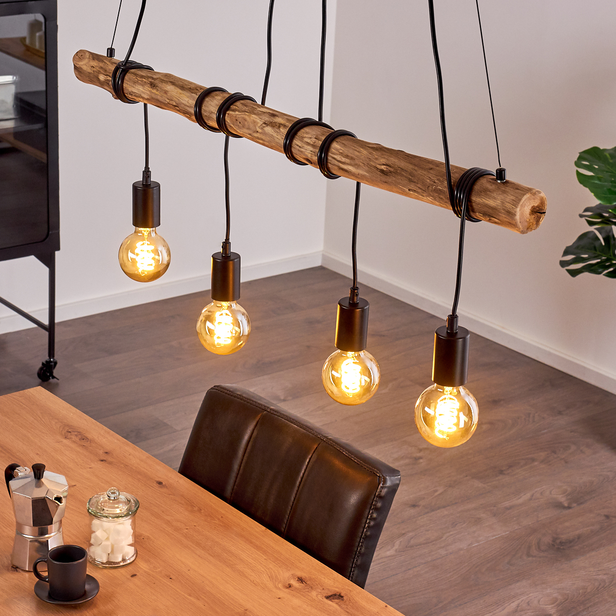 Eine Hängelampe aus einem Holzstamm mit vier Glühbirnen über einem Holztisch.