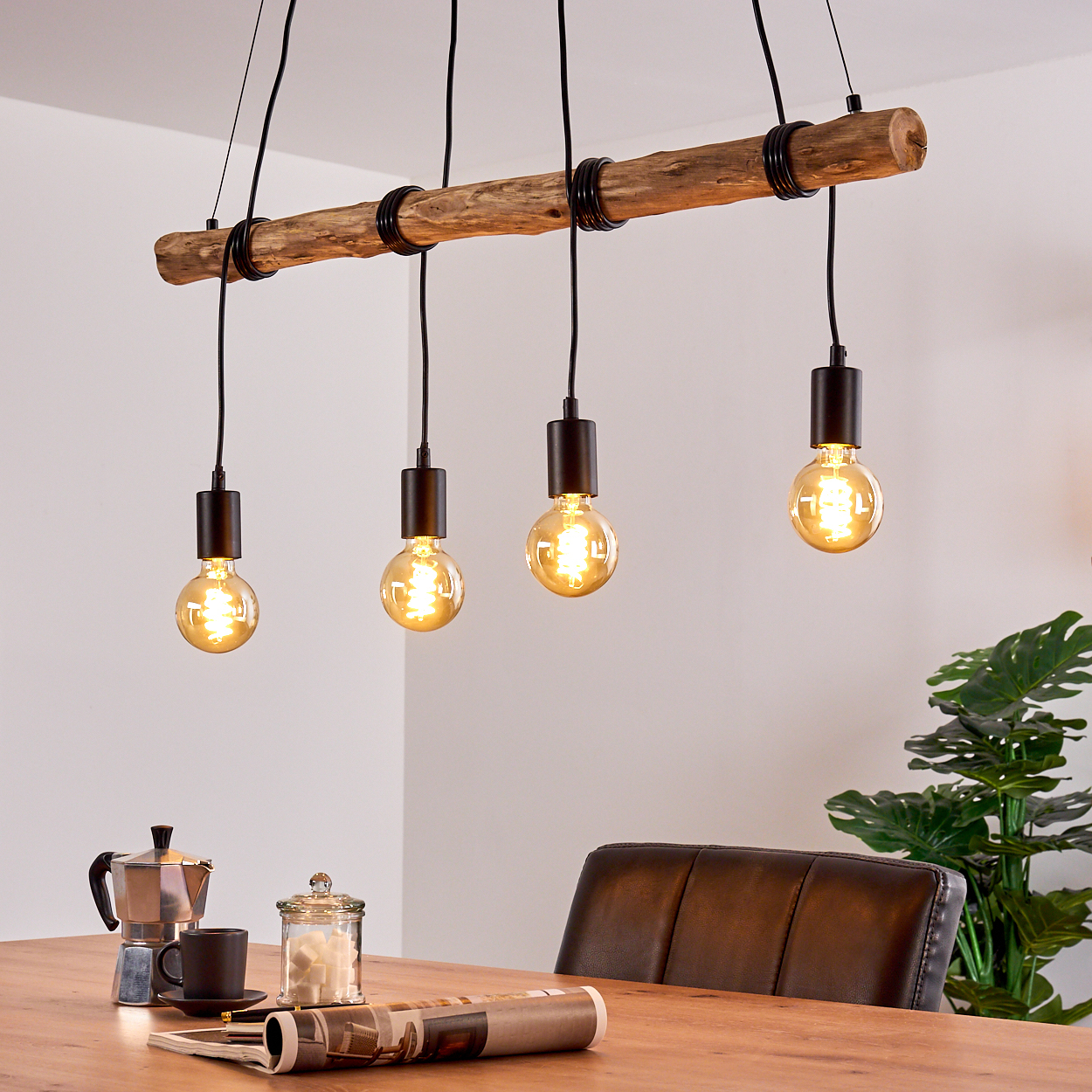 Eine rustikale Pendelleuchte mit vier Glühbirnen hängt über einem Holztisch.