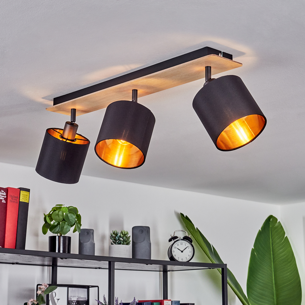Deckenlampe mit drei schwarzen Schirmen und goldenem Inneren.