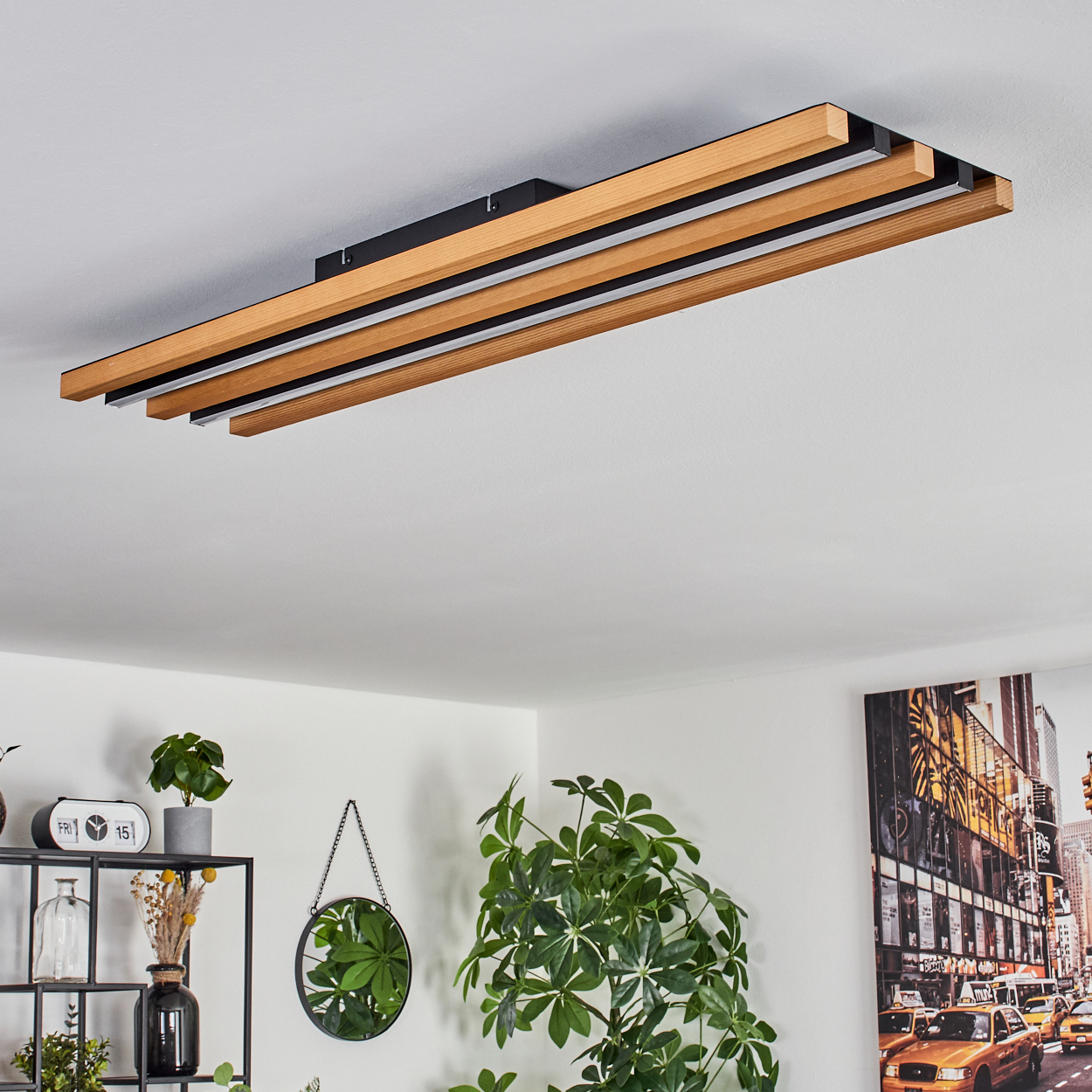 Deckenleuchte mit Holzlamellen und LED-Streifen, über einem Regal mit Pflanzen und Kunstwerk.