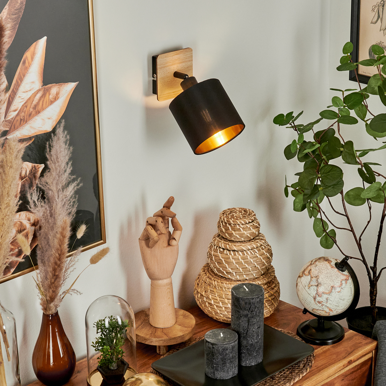 Ein schwarzer Wandspot mit Holzsockel beleuchtet einen Nachttisch mit Deko.