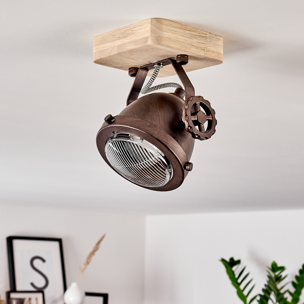 Eine kupferfarbene Lampe mit Holzsockel hängt an der Decke. Ein Rad ist am Lampenschirm.