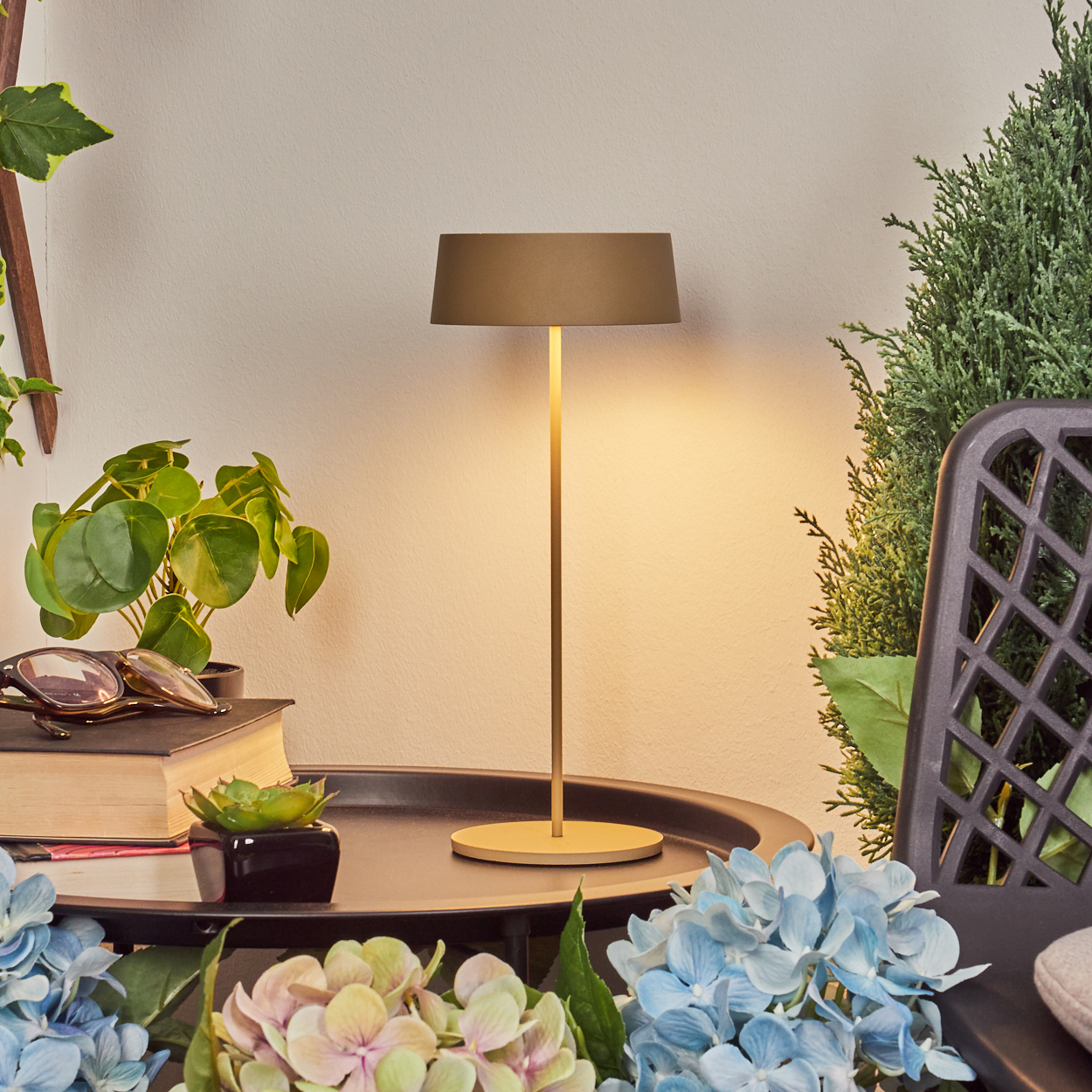 Ein goldener Tischlampe auf einem Tablett mit Pflanzen und Blumen.
