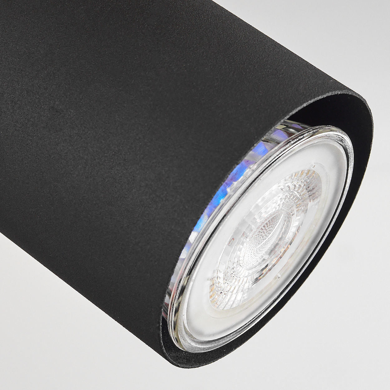 Eine schwarze zylindrische Leuchte mit Glaslinse, die eine helle LED-Birne zeigt.