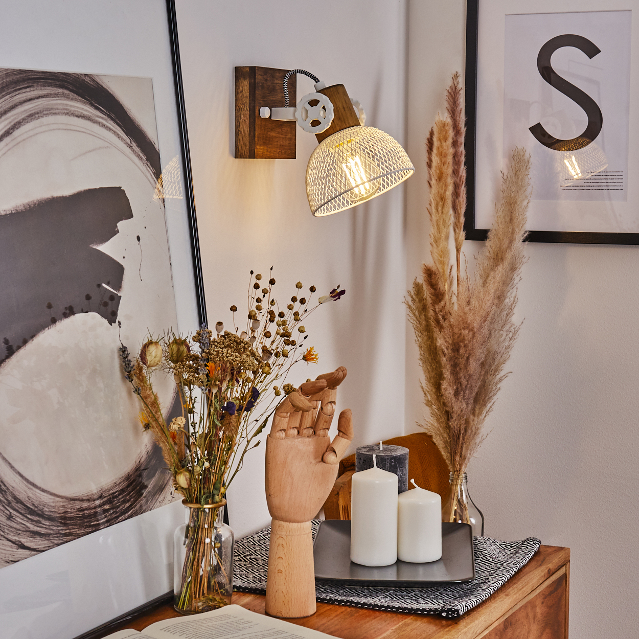 Holzhand, Trockenblumen, Kerzen und Lampe auf einem Nachttisch.